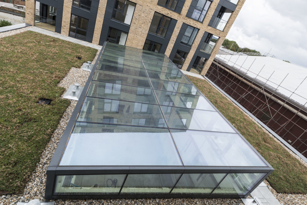 A modern building with a large structural atria glazing roof extension and green roofing, featuring gravel and brick exterior walls.