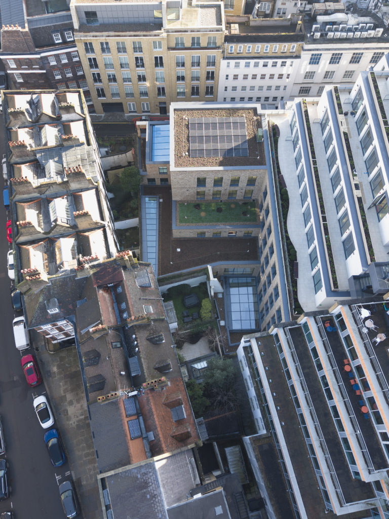 Aerial view of city buildings and streets, featuring rooftops with bespoke commercial rooflights, parked cars, solar panels, and a central courtyard with greenery.