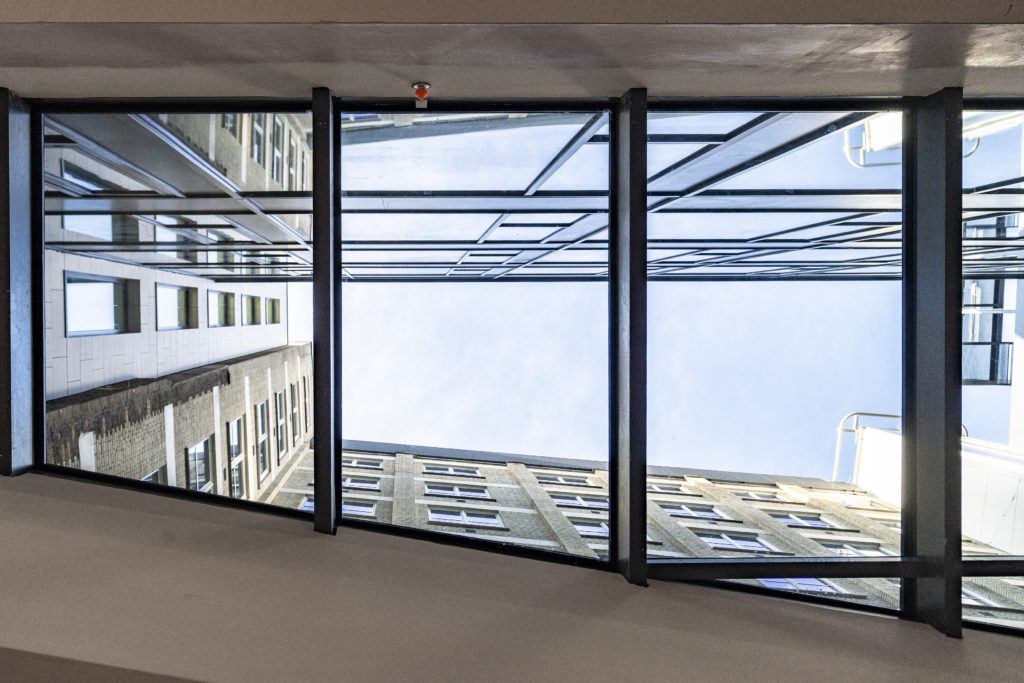 View looking up at two tall buildings separated by a glass skybridge, with reflections of the structures visible in bespoke commercial rooflights above.