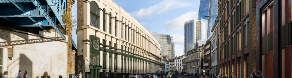 A city street with old and modern buildings, parked cars, pedestrians, and a blue railway bridge crossing above on the left features bespoke atrium rooflights illuminating a contemporary façade.