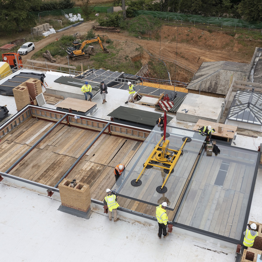 Construction workers install large glass panels on a building under construction. Heavy machinery and building materials are visible in the background.