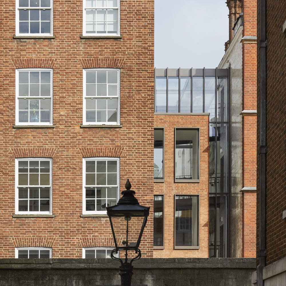 1000-Morey Smith_Blackstone Chambers_London_©Hufton+Crow_003 View of multi-story brick buildings with white-framed windows and a modern glass extension in between. A vintage streetlamp is visible in the foreground.