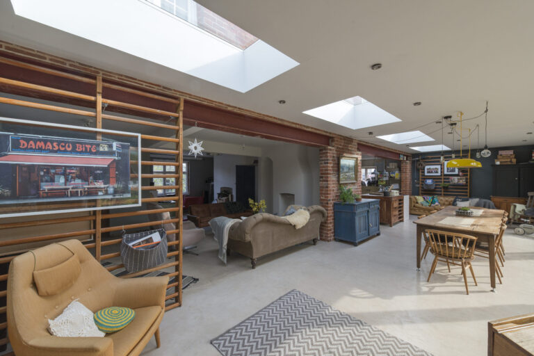Spacious, open-plan living area with skylights, eclectic furniture, a mix of modern and rustic decor, and a large wall-mounted photo of a store named "Damasco Bites.