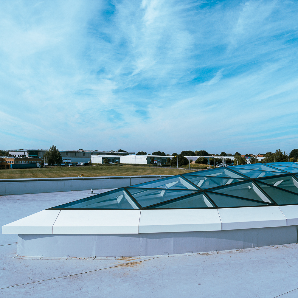 A rooftop with geometric glass panels, set against a backdrop of blue sky and distant buildings.