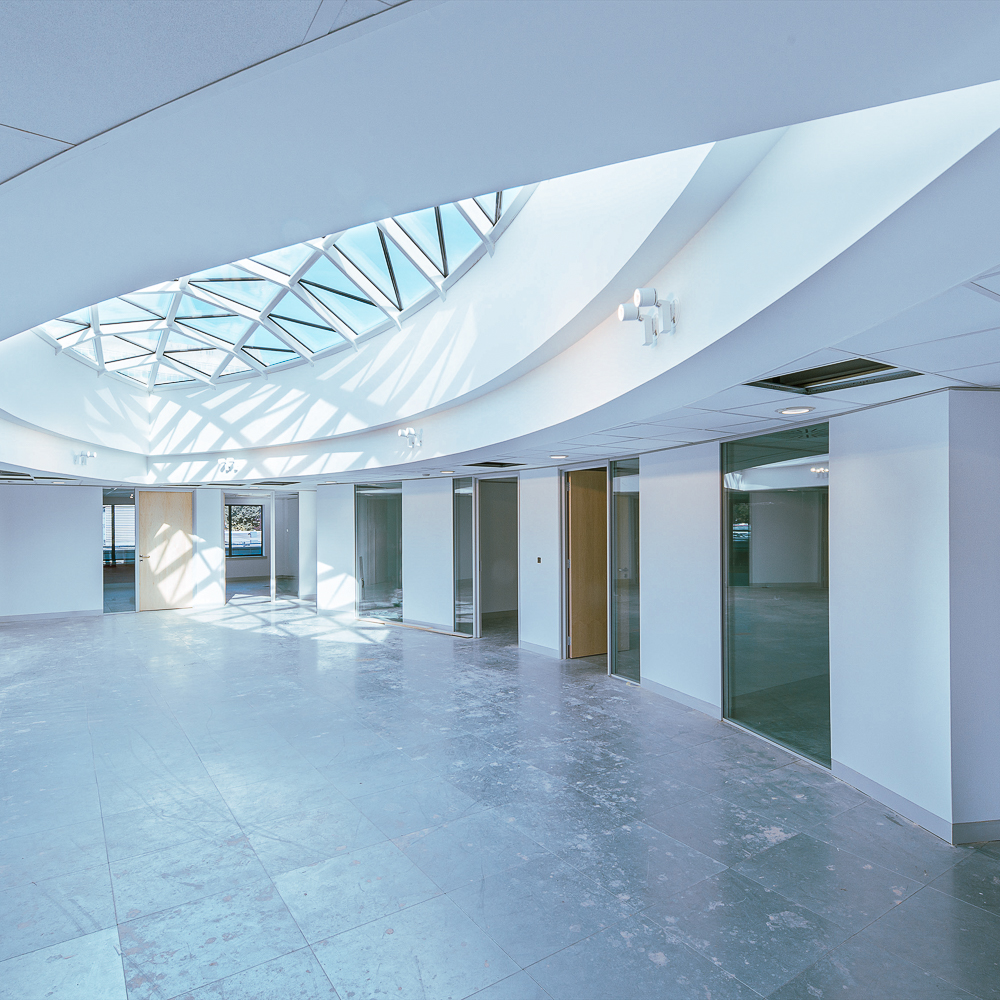 Spacious modern office interior with large skylight, glass doors, and tiled floors.