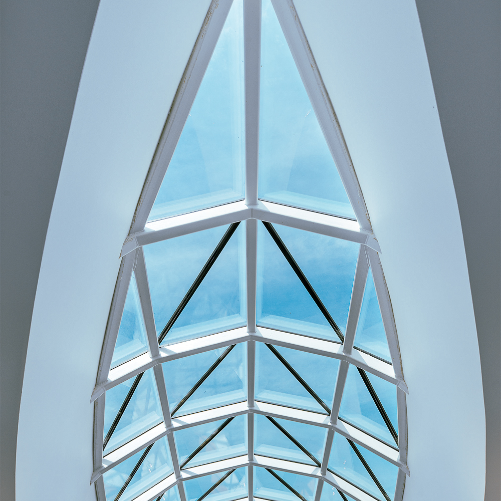 Geometric glass ceiling with triangular panels and blue sky visible through them.