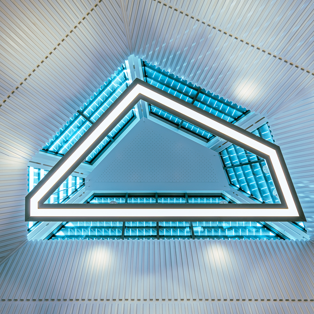 Geometric ceiling design with blue-lit triangular light fixture and white panels.