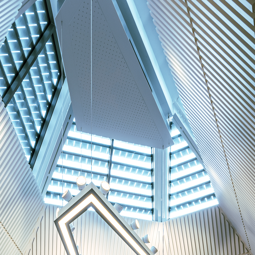 Modern architectural ceiling with triangular shape, featuring striped panels and geometric lighting.