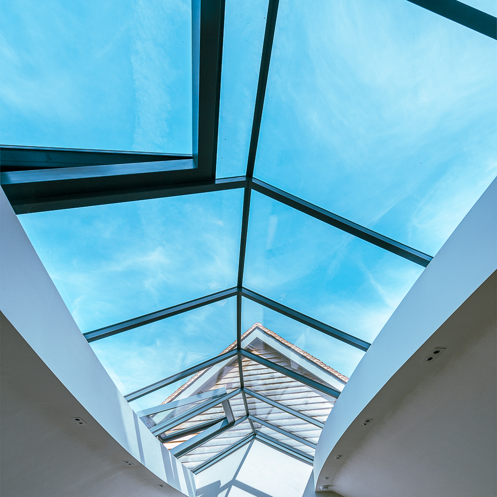 View of a geometric glass ceiling with blue sky visible, framed by white interior walls.