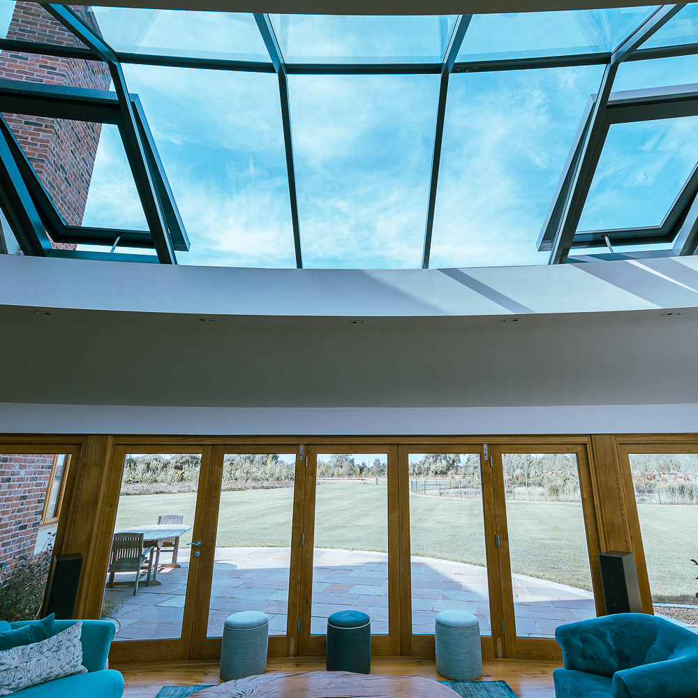 Spacious room with large skylight, glass doors, blue furniture, and a view of a grassy field and trees.