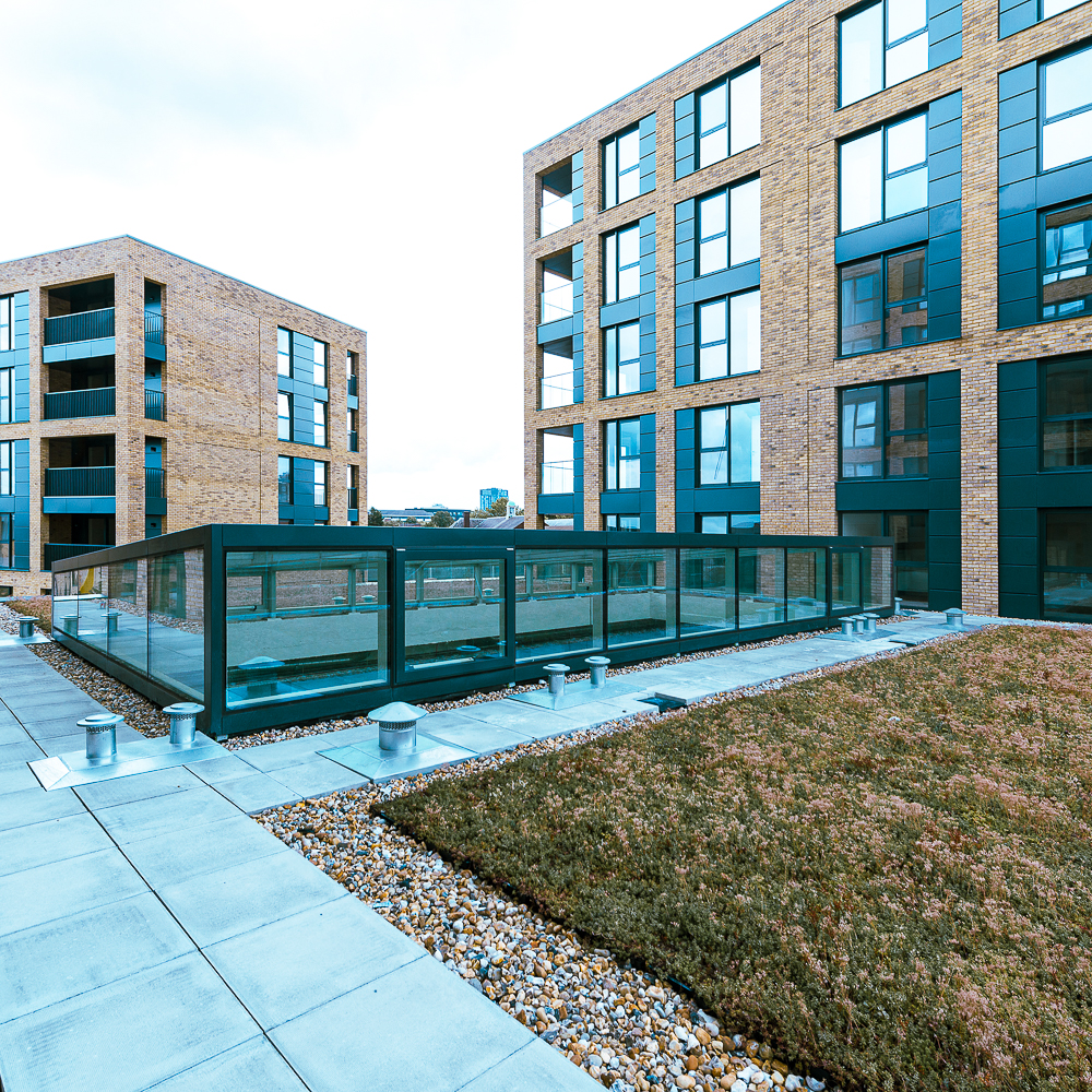 Modern apartment buildings with brick and glass facades surround a landscaped rooftop garden and walkway area.