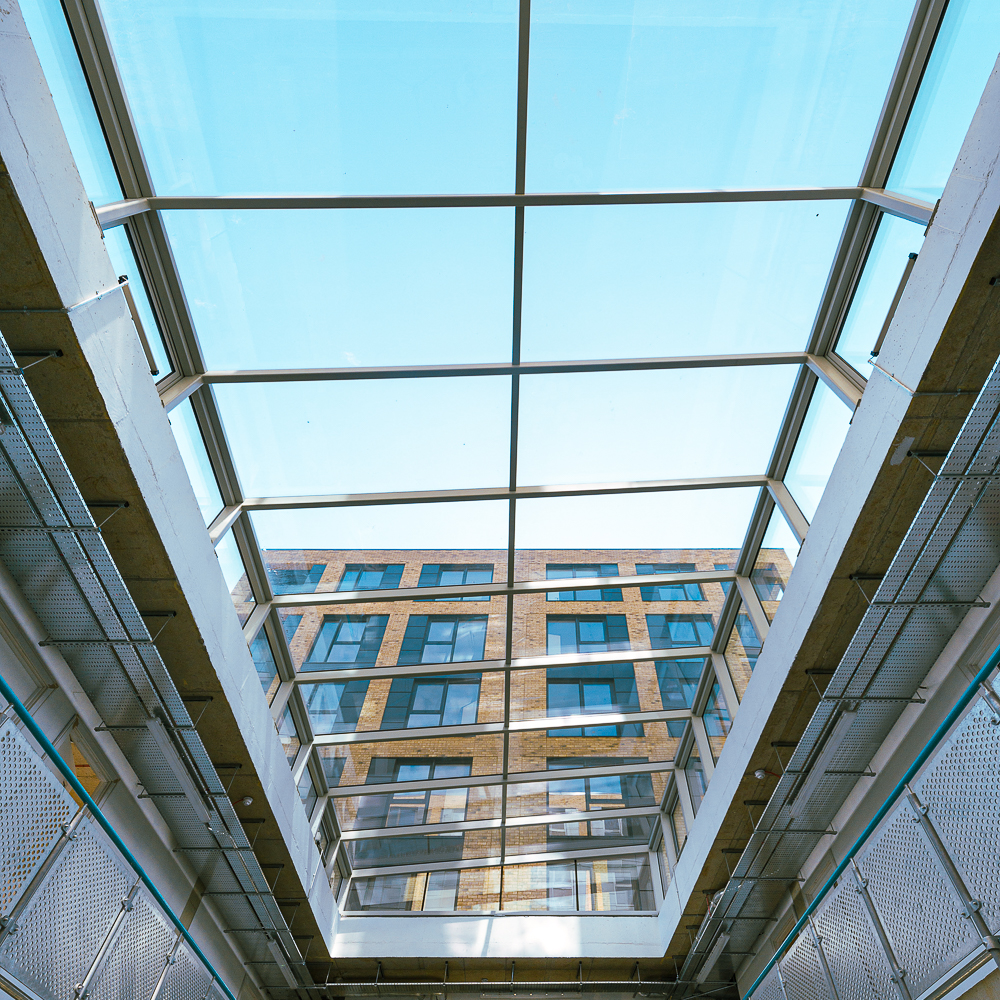 View from below of a modern building with a large glass ceiling, showcasing a clear blue sky and the facade of the structure.