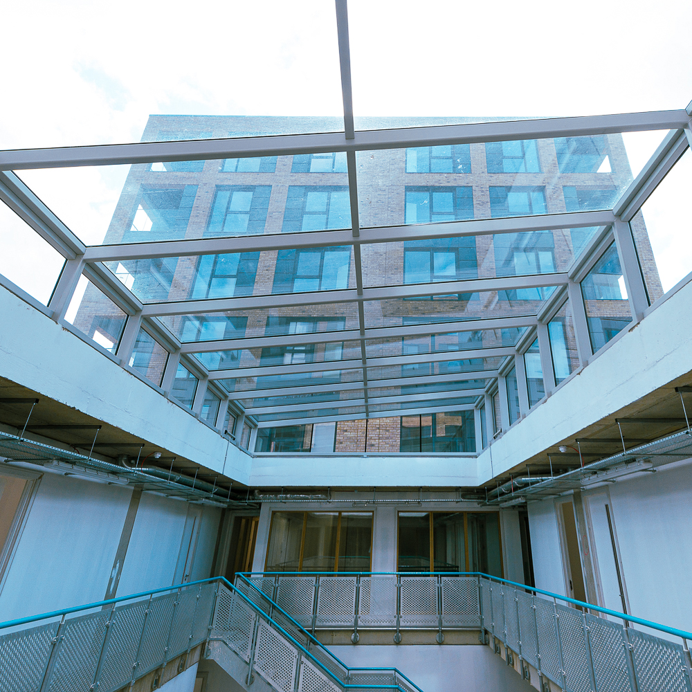 View from a building's interior courtyard looking up at a glass ceiling and a multi-story brick building in the background.