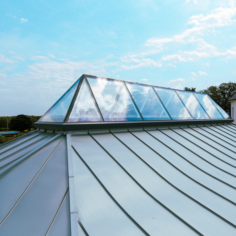 A metal roof with a row of triangular glass skylights under a bright blue sky.