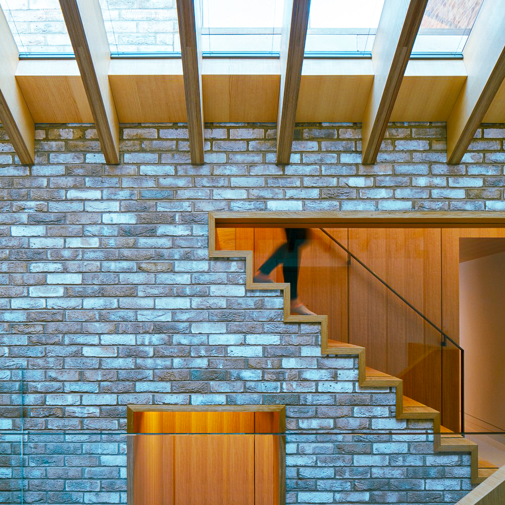 A person descends a wooden staircase inside a building with exposed brick walls and wooden ceiling beams.