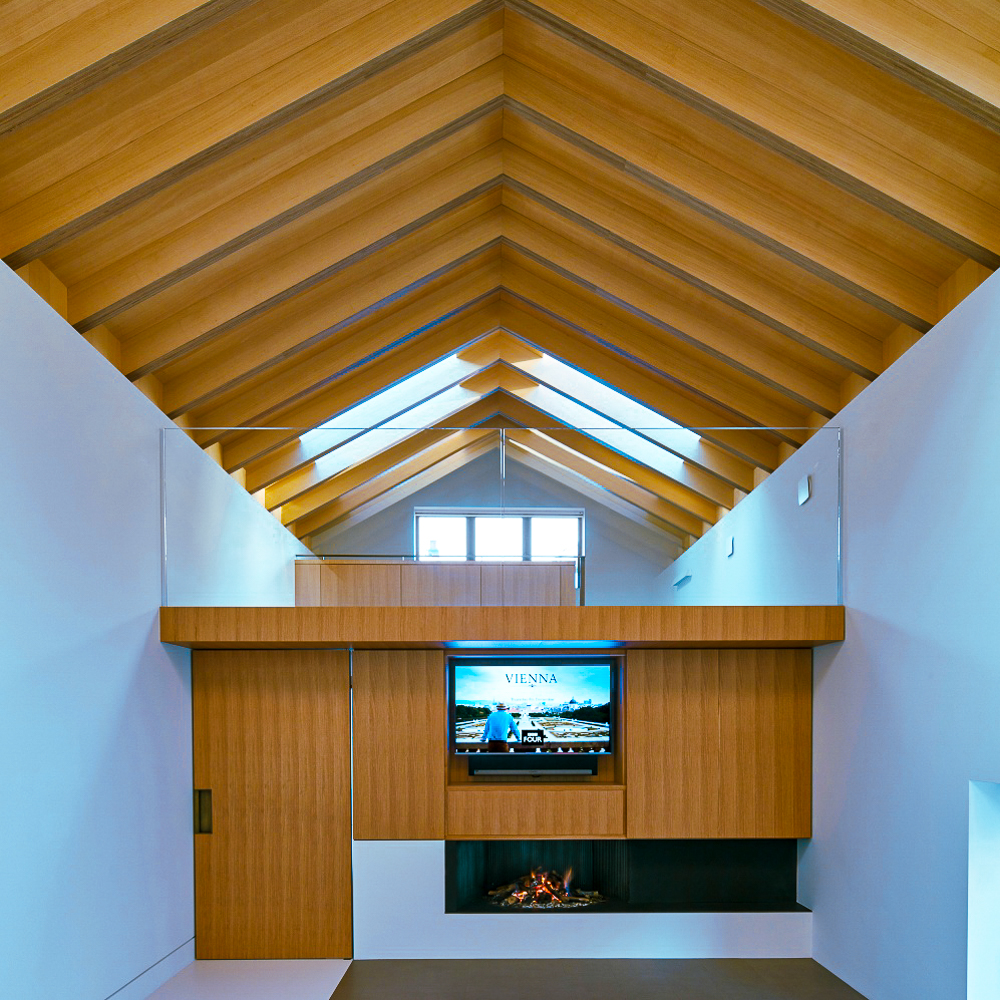 Modern living room with a wooden vaulted ceiling, a fireplace, and a TV displaying an image above the mantel.