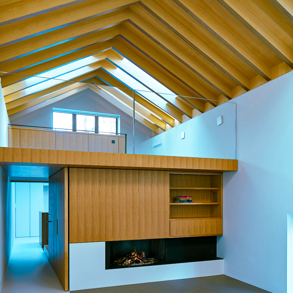 Modern interior with a vaulted wooden ceiling, a loft area, and built-in wooden cabinetry housing a decorative fireplace. Natural light enters through a skylight.
