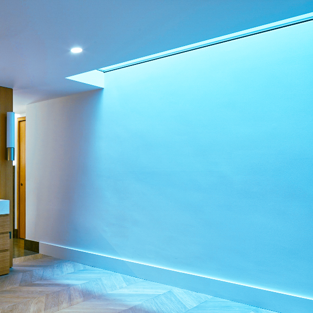 A modern interior with a blue-lit ceiling and wooden flooring. A partial view of a wooden cabinet and a doorway is visible on the left.
