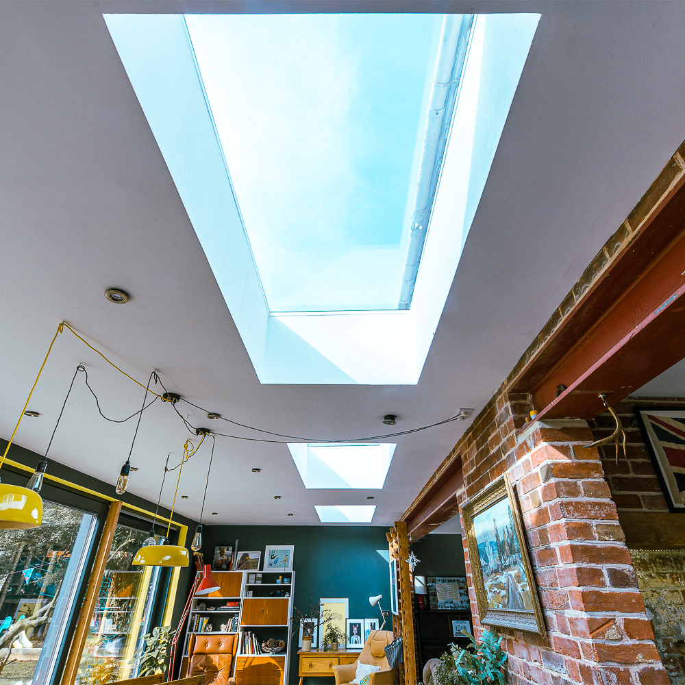A room with angled skylights, brick wall, and blue-painted wall. It features shelves, framed pictures, and yellow pendant lights hanging from the ceiling.