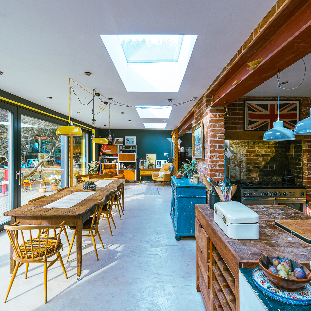 Bright, eclectic kitchen and dining area with skylights, brick accents, colorful decor, and a Union Jack on the wall.