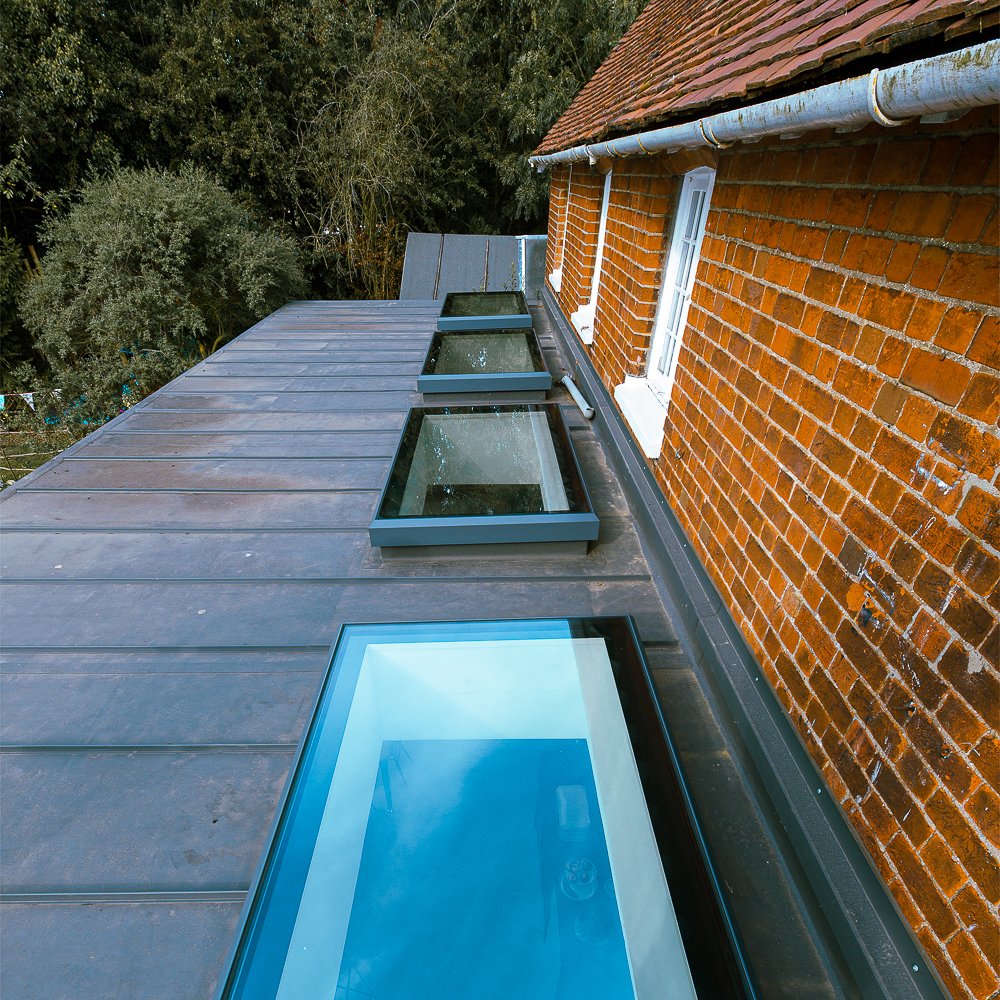 Rooftop view of a building with multiple skylights and a brick exterior, surrounded by dense greenery.