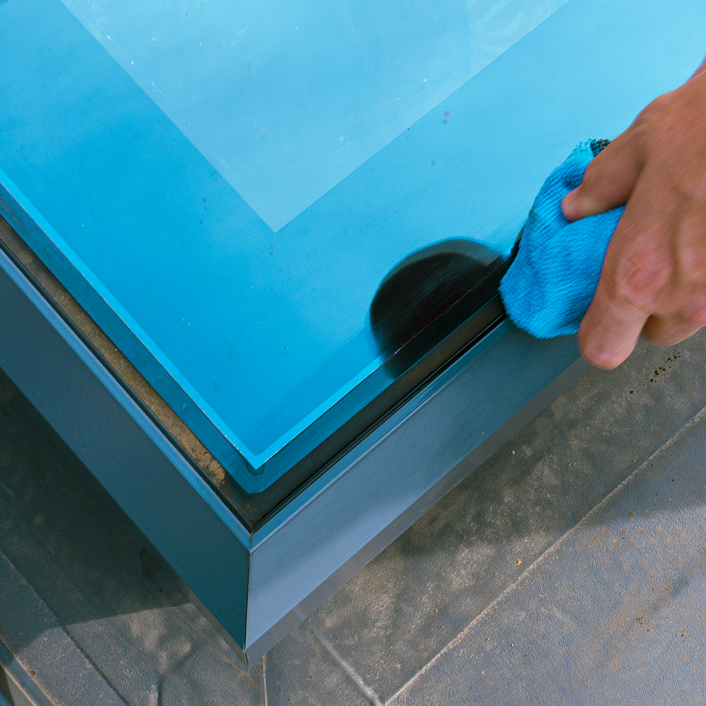 A person cleans the edge of a blue glass panel with a blue cloth.