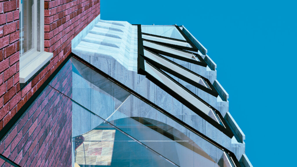 Glass-roofed extension with black frame, attached to a red brick building against a clear blue sky.