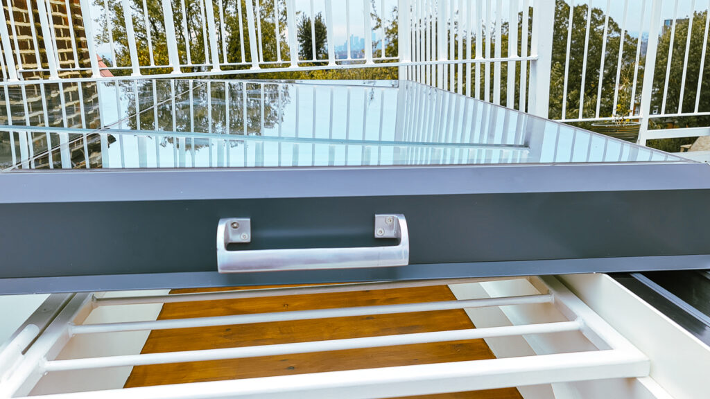 A solar panel installed on a rooftop with a metal railing and trees visible in the background.