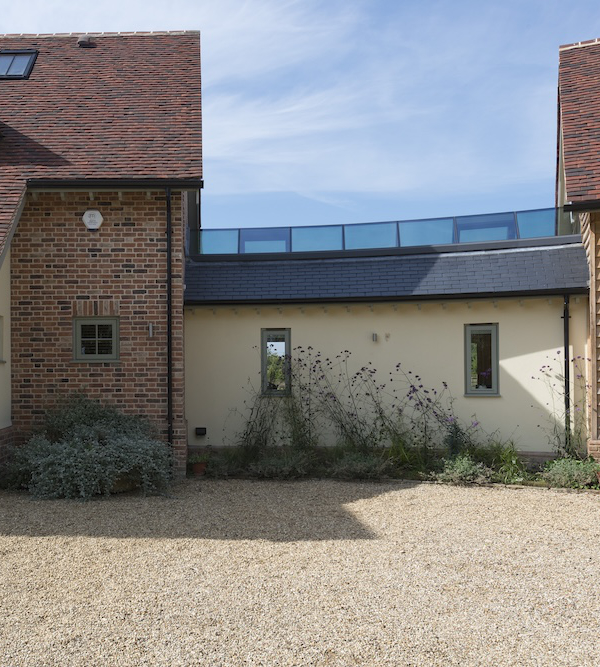 A building with red brick and beige walls, featuring small windows and a glass extension on the roof, surrounded by gravel and vegetation.