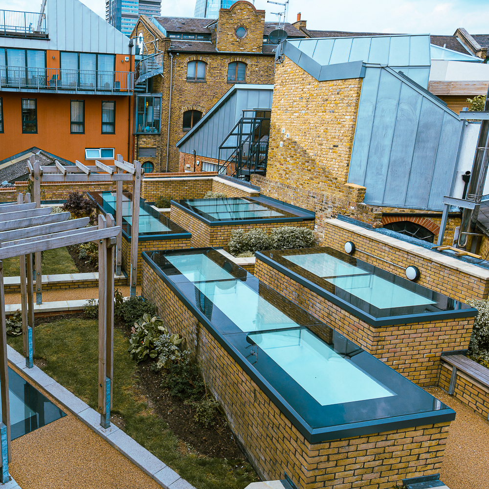 A rooftop garden with brick planters, glass covers, and surrounding modern and rustic buildings.