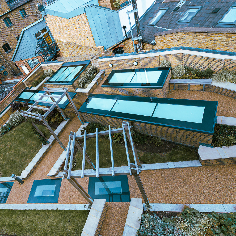 A rooftop garden with walkways, modern pergolas, and skylights set among brick buildings.