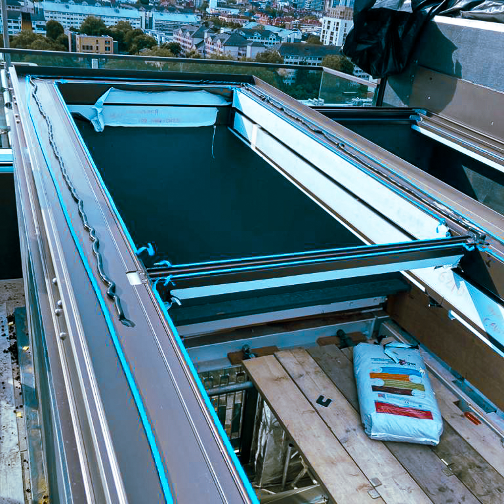 A rooftop pool under construction with visible framing, insulation, and a bag of materials nearby. Urban skyline in the background.