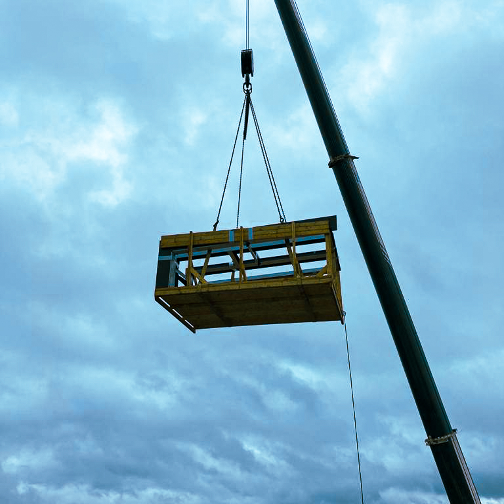 A large crane lifts a wooden frame against a cloudy sky.
