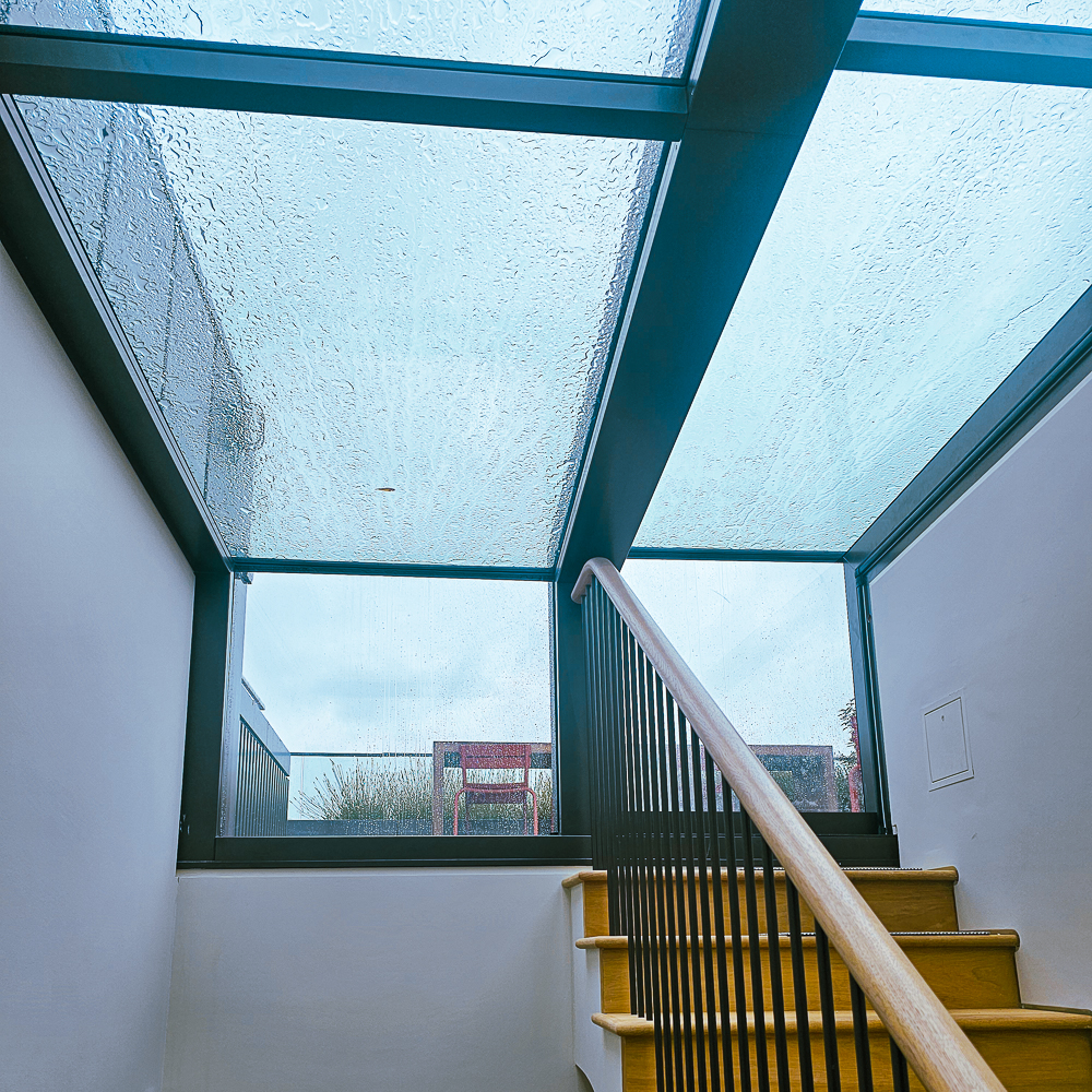 Staircase leading up to a large glass ceiling with raindrops. The sky is overcast, and some greenery is visible outside.