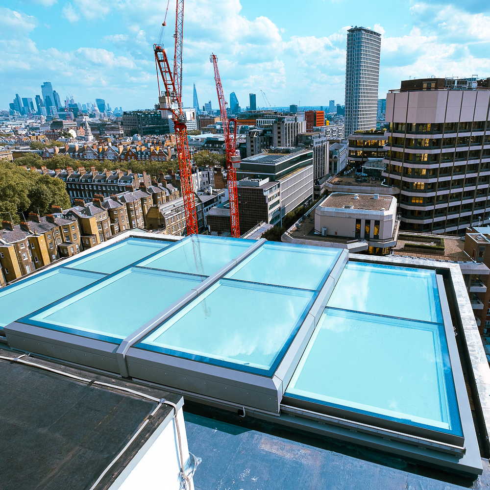 A rooftop with large glass panels overlooks a cityscape with high-rise buildings and red cranes in the background.
