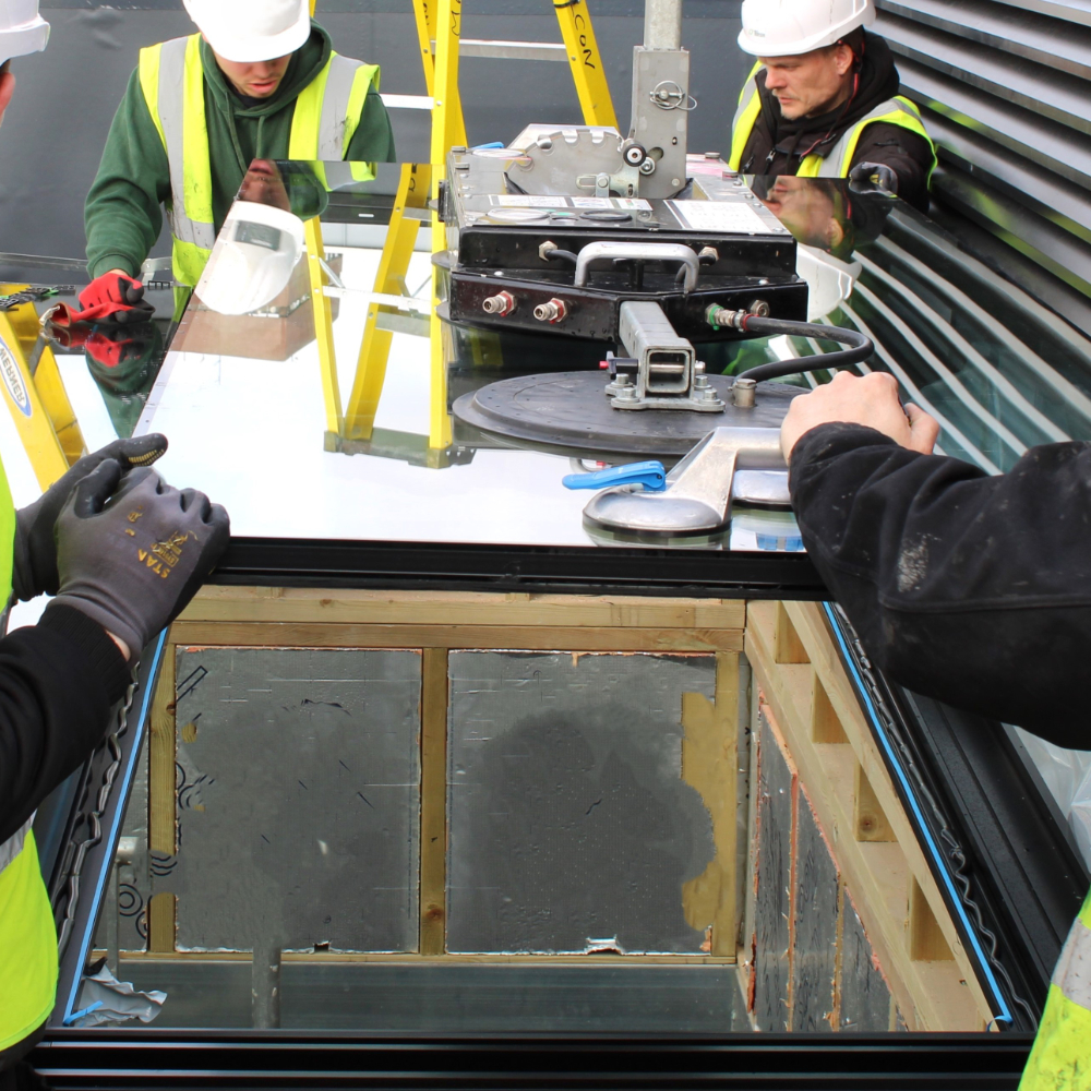 NGR Rooflight Installation with Crane and Installation Team Workers in high-visibility vests and hard hats install a large windowpane using suction lifters and other equipment at a construction site.