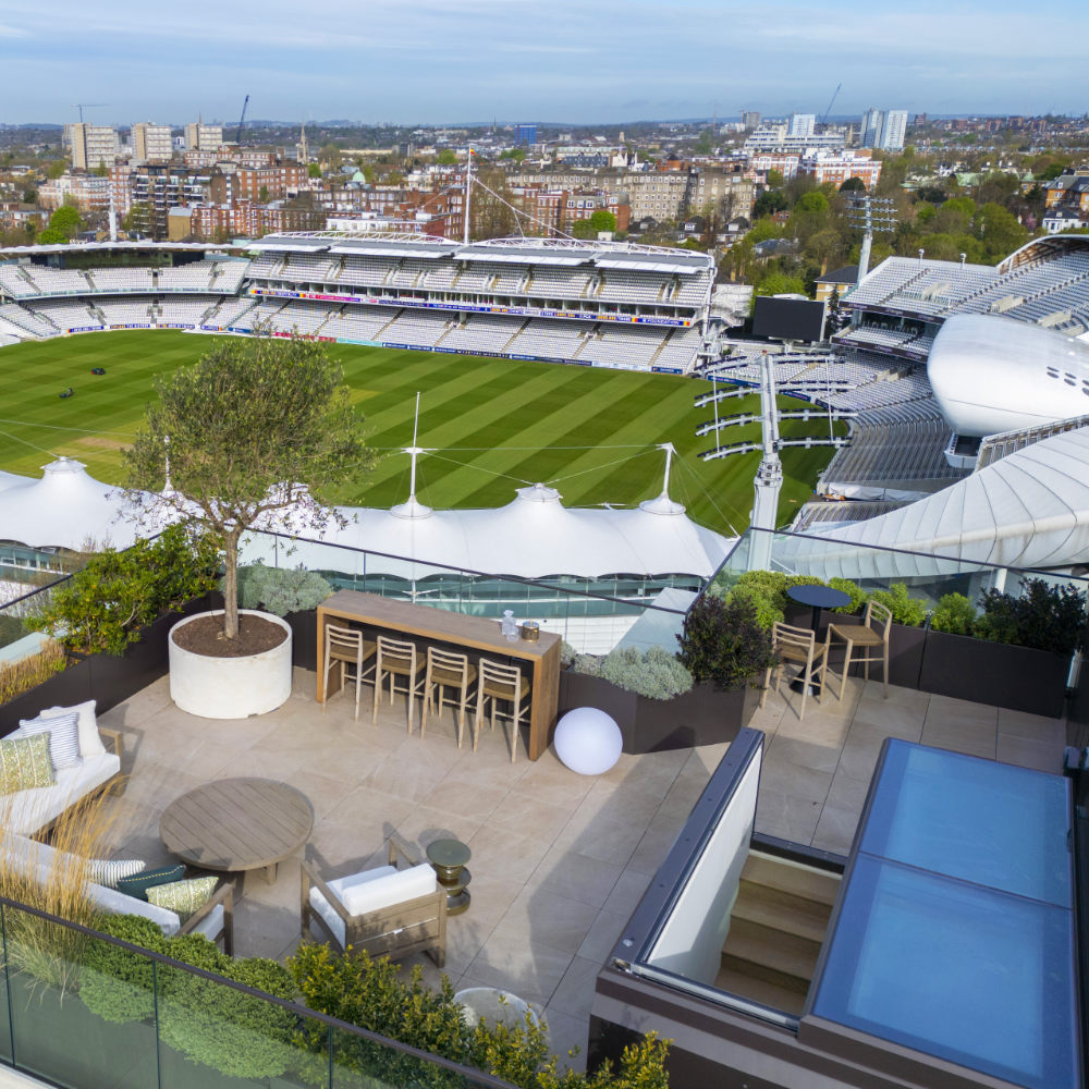 NGR Sliding Box Rooflights High End Residential Project London A rooftop terrace overlooking a green sports stadium with seating, a tree in a planter, outdoor furniture, and a clear day.