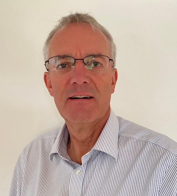 A man with short gray hair, wearing glasses and a white striped shirt, is looking at the camera. The background is plain white.
