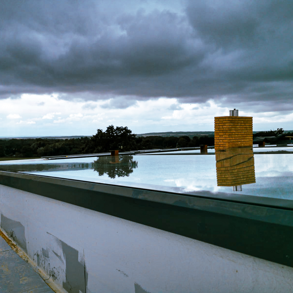 Flat roof with a reflective surface, a yellow brick chimney, and cloudy sky in the background.