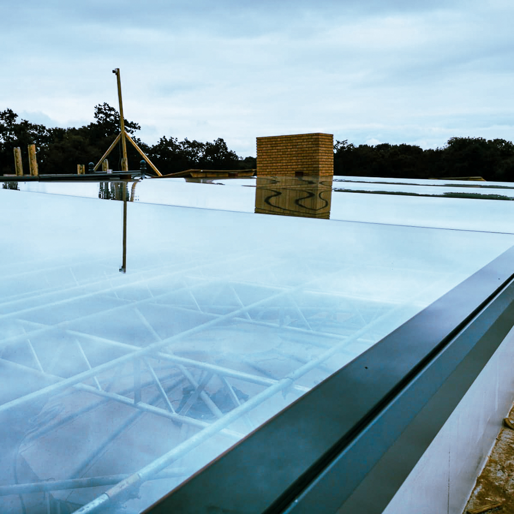 Glass roof with visible metal framework beneath, reflecting the cloudy sky and surrounding trees.