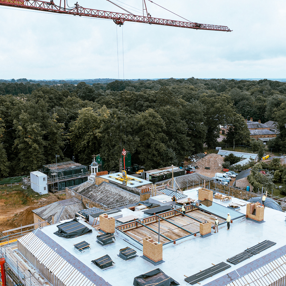 Aerial view of a construction site with a crane, workers on a rooftop, and surrounding trees and buildings.
