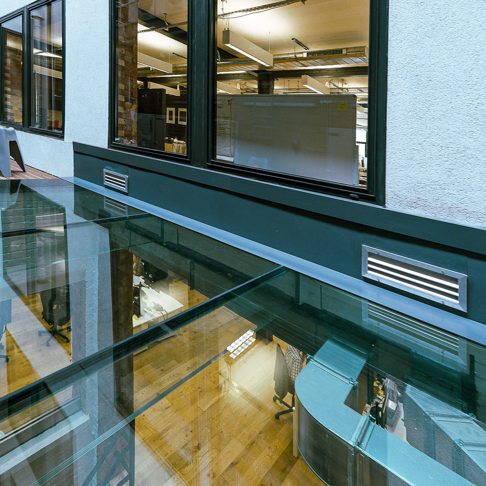 View of an interior office space through a glass ceiling, showing desks and chairs below.