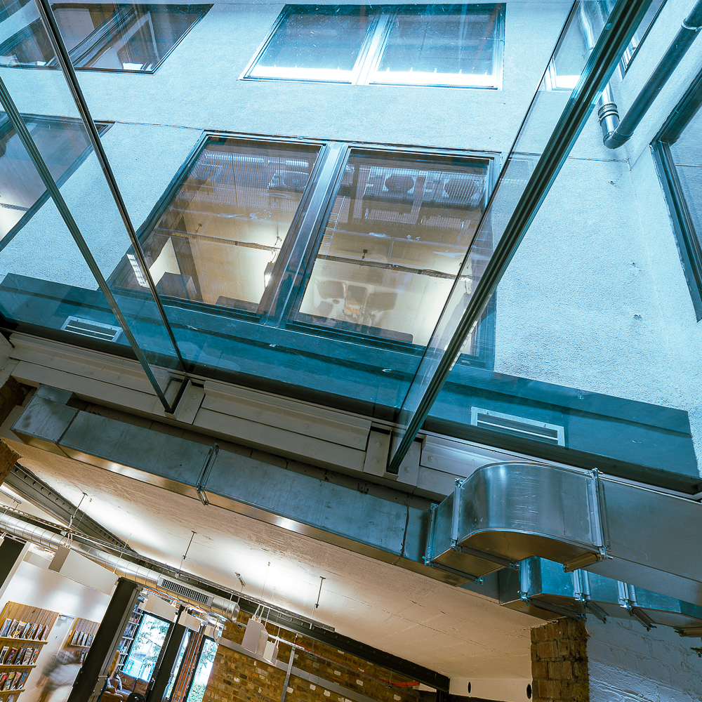 Modern interior with a glass ceiling, exposed ducts, large windows, and brick wall accents.