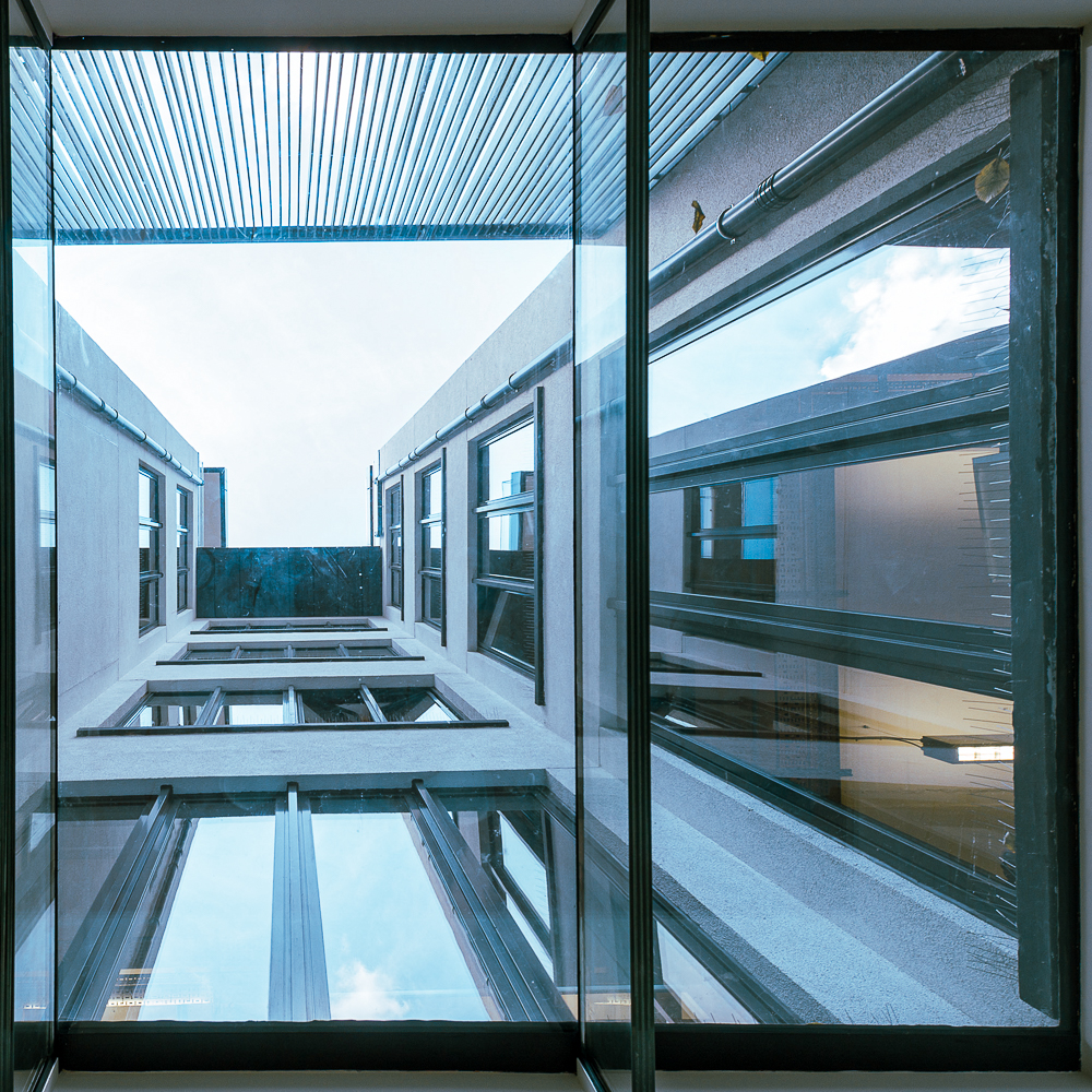 View from below of a modern glass and concrete building with multiple windows, reflecting the sky.