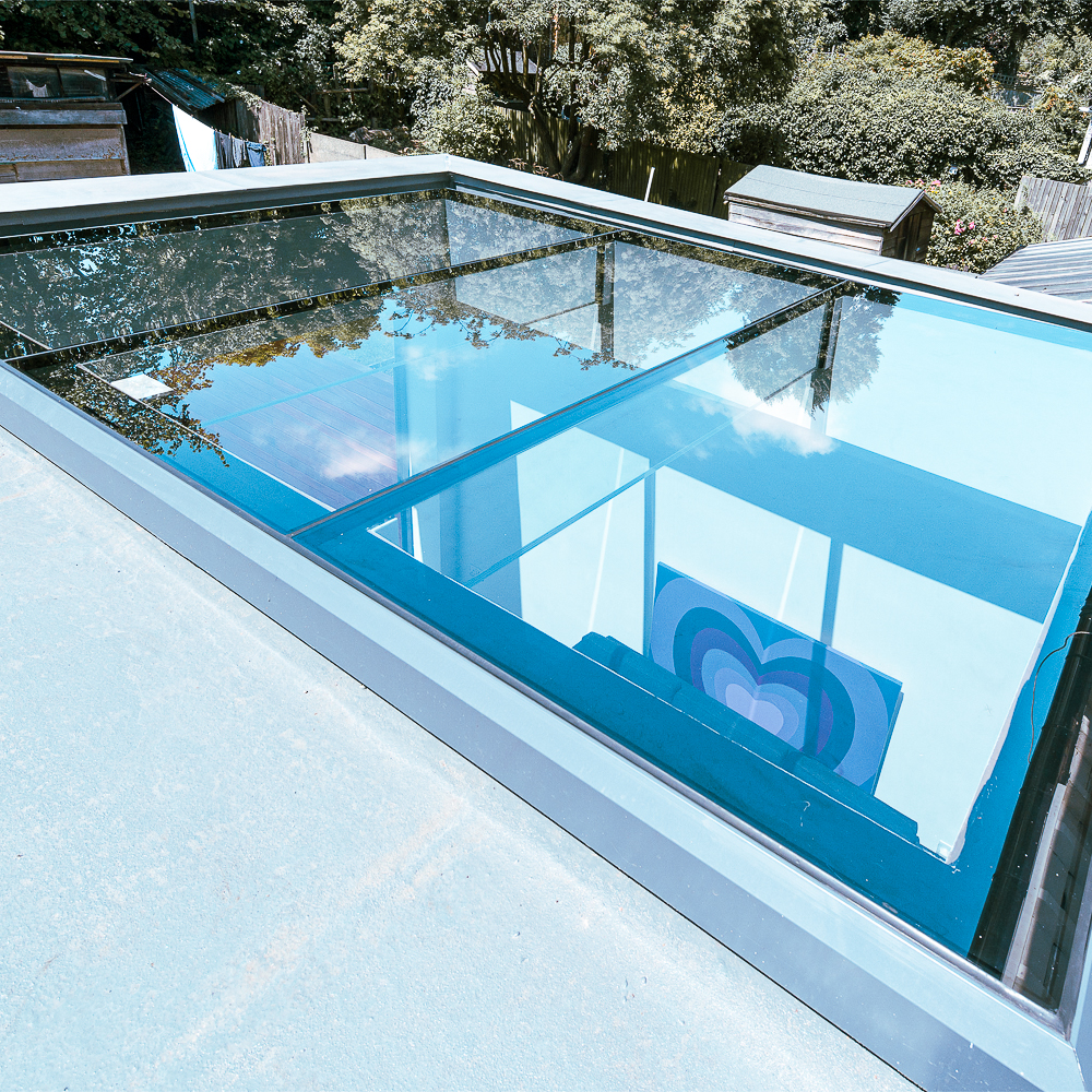 A large glass skylight with a blue tint reflects the sky and nearby trees. A colorful design is partially visible below the glass.
