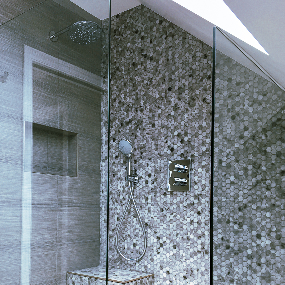 Modern shower with glass enclosure, rainfall showerhead, and handheld shower set against a hexagonal tile wall.