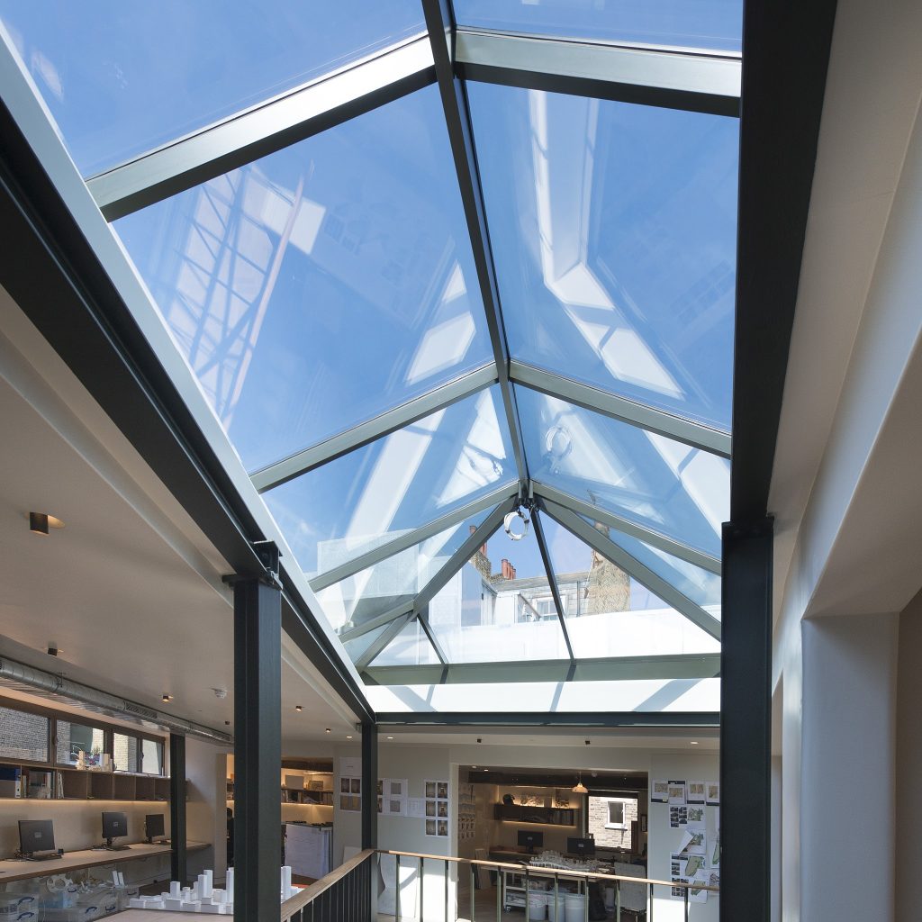 A modern ceiling with large triangular glass panels allowing natural light into the interior space below, which includes shelves and displays.