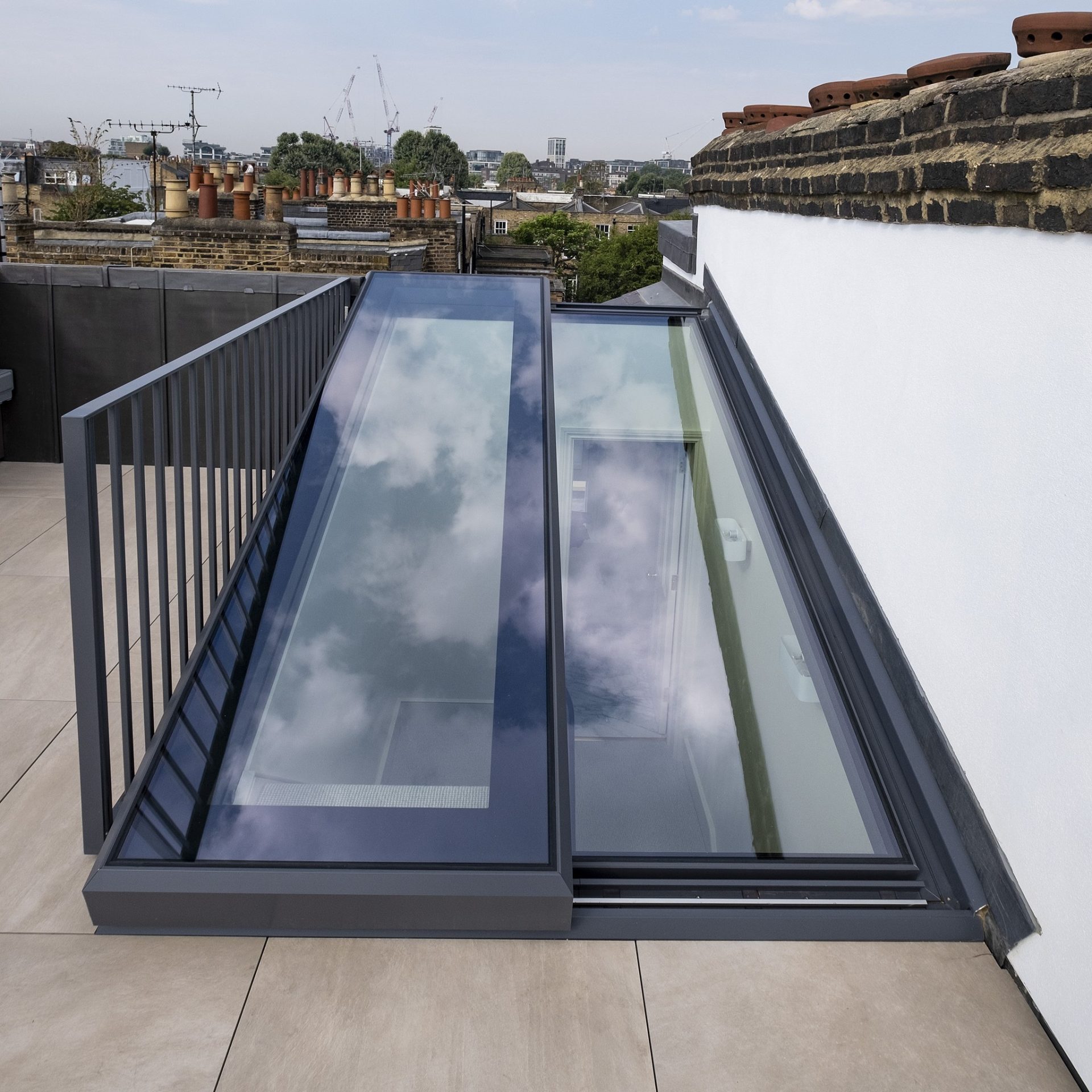 A modern rooftop with large glass skylights reflecting the sky, surrounded by railings and an urban cityscape in the background.