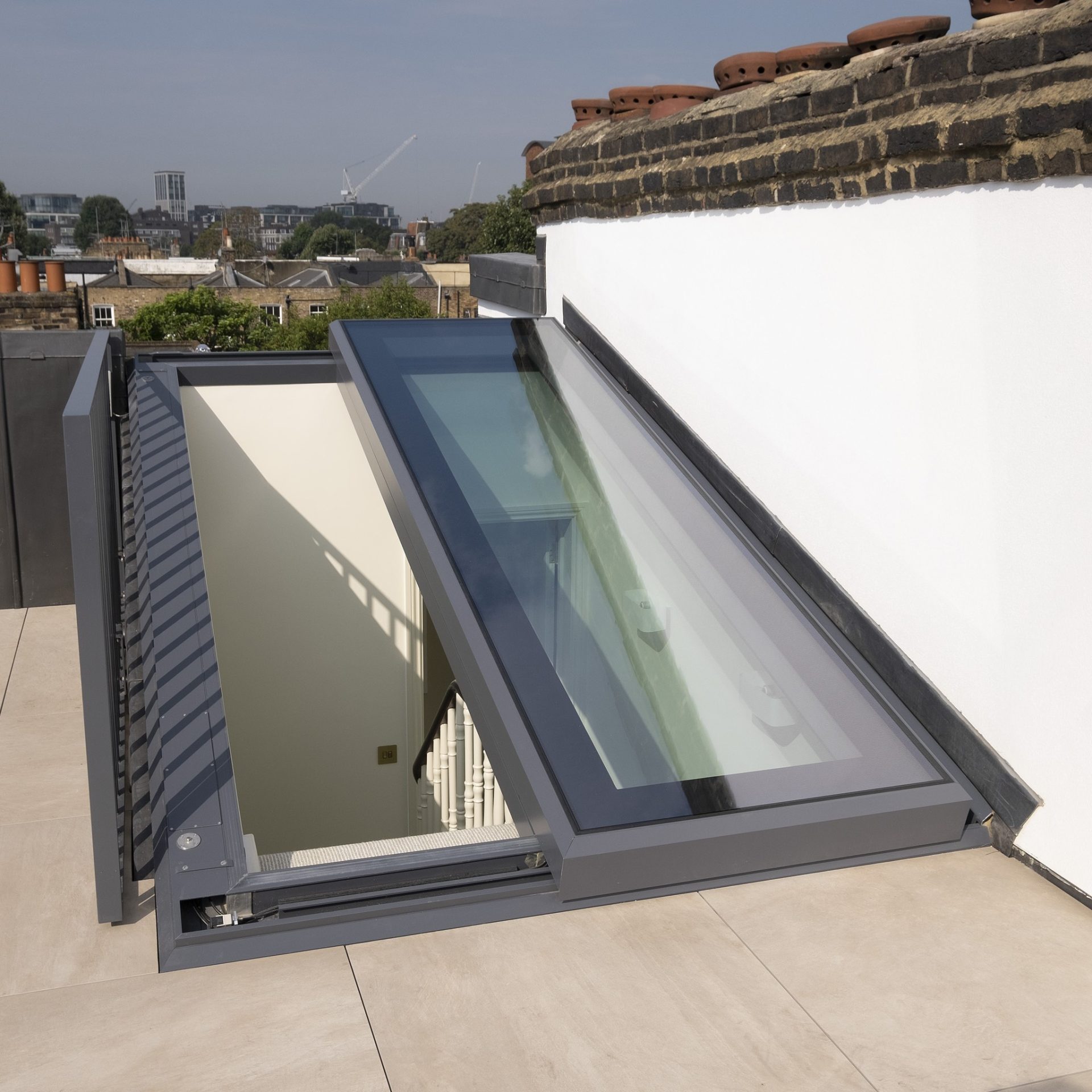 A modern rooftop with a glass panel entryway and terracotta chimney pots against a blue sky with clouds.