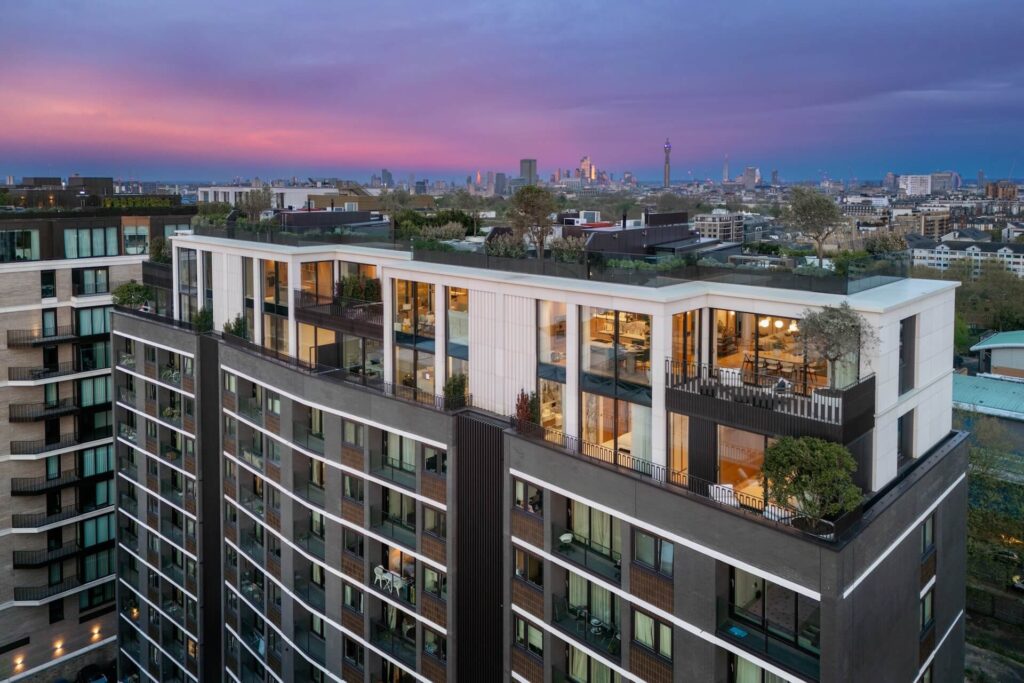 High-rise building with rooftop terraces, surrounded by cityscape, under a purple and pink sky during sunset.